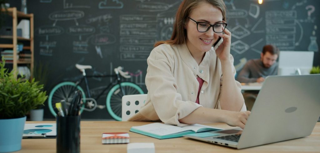 Woman talking on phone while working on laptop in office