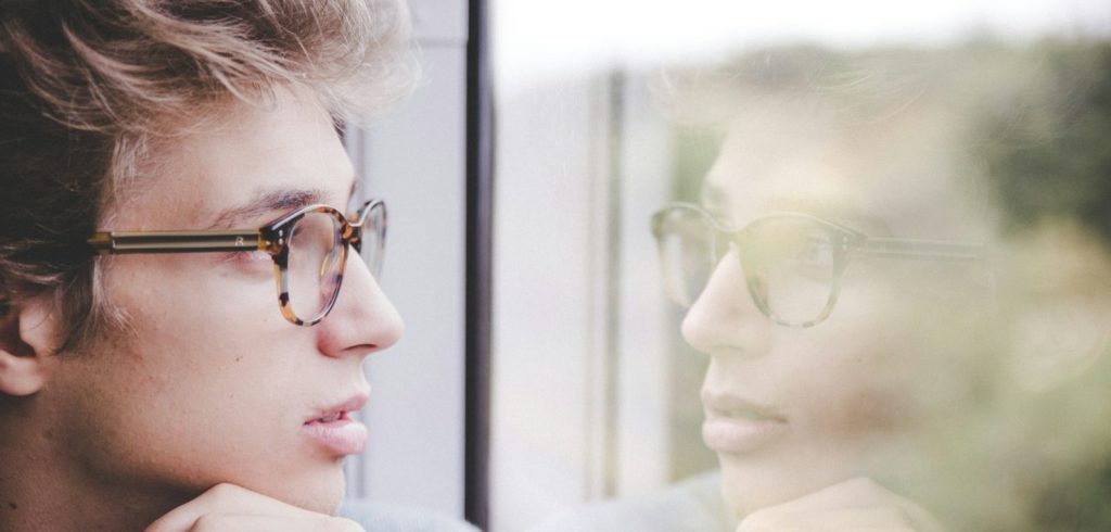 A man wearing glasses looking out a window